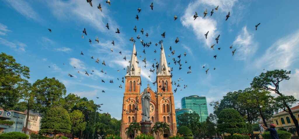 pexels-photo-1018478-1018478 Flock of birds flying over Notre-Dame Cathedral Basilica Saigon in vibrant daylight.